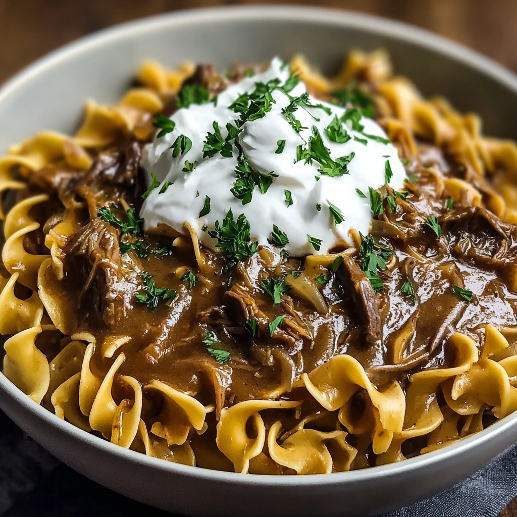 cozy crock pot french onion beef and noodles on a plate with garnish